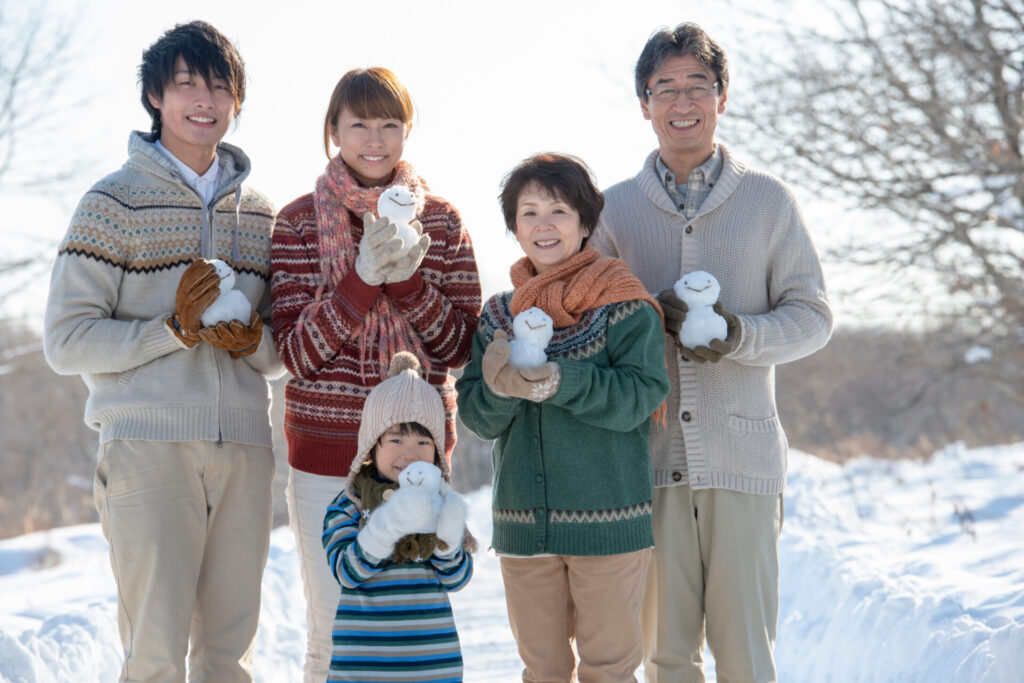 会社の福利厚生制度を利用して旅先で雪だるまを持ち微笑む3世代家族